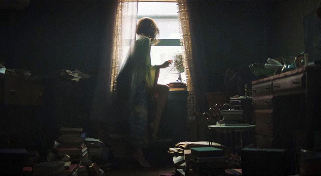 June Leigh observa da janela o movimento da rua.