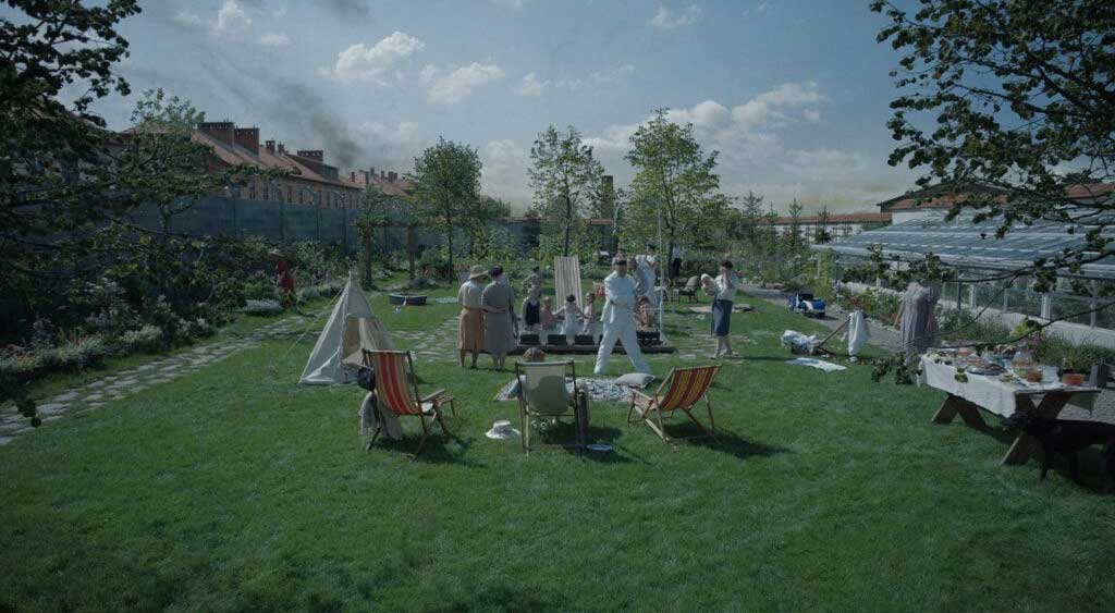 Família Höss no luxo de seu quintal e ao fundo as chaminés de Auschwitz-Birkenau expelem fumaça.