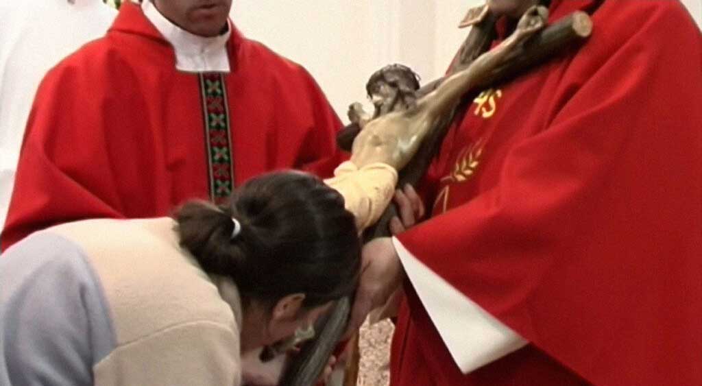 Clare Crockett se inclina para beija os pés de Jesus Crucificado.