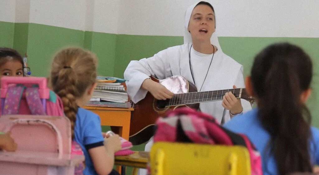 Ir. Clare toca violão para acalmar as crianças, após retornarem à sala de aula mais agitadas.