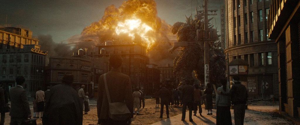 A população observa Godzilla frente a destruição causada após atacar a cidade com um raio atômico.
