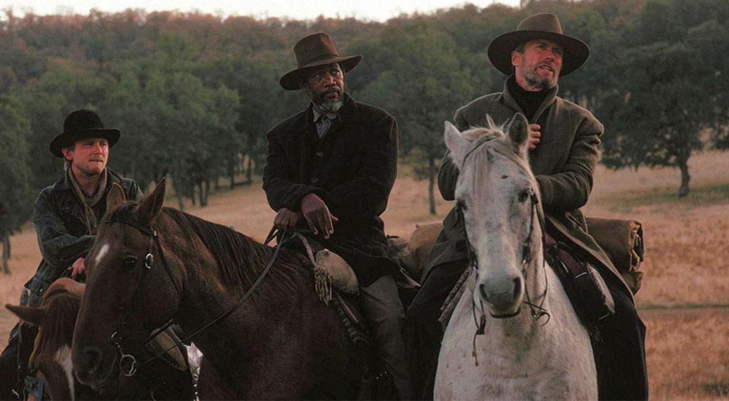 Schofield Kid, Ned Logan e William Munny montados em seus cavalos.