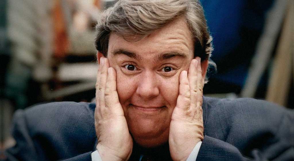 John Candy com as mãos erguidas ao lado do rosto em uma expressão de surpresa. Ele era gigante como comediante.