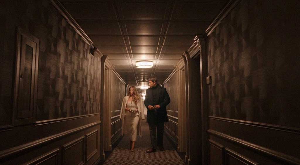 Millie e Andrew caminham pelo corredor do hotel até seus quartos.